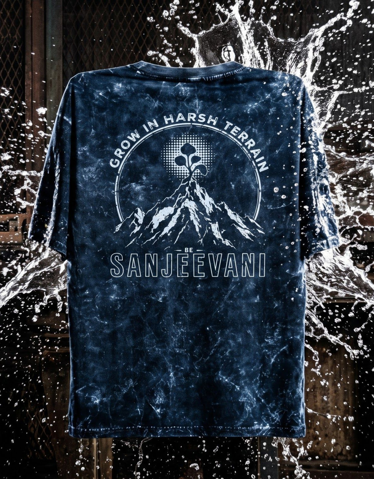 A dark navy blue short-sleeve acid wash t-shirt, featuring a mountain and a ethereal flower with the text 'GROW IN HARSH TERRAIN' and 'SANJEEVANI'. The shirt is displayed against a dark background with a water splash effect.